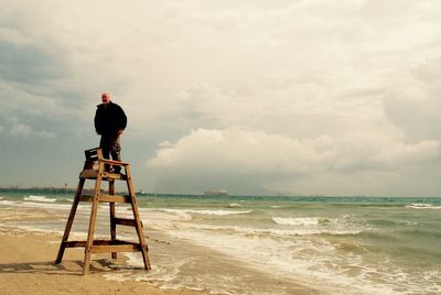 Man standing on lifeguard chair at beach