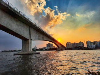 Bridge over river by buildings against sky during sunset