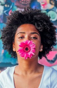 Portrait of woman with pink gerbera daisy in mouth against graffiti wall