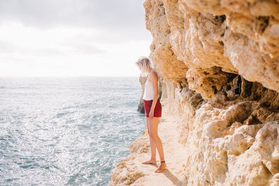 Woman standing on rock by sea against sky