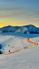 Scenic view of mountains against cloudy sky during winter at sunset