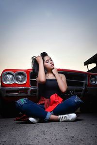 Woman sitting on car against sky