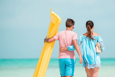 Rear view of couple walking on beach against sky