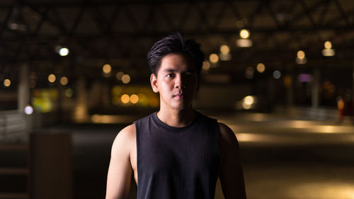 Portrait of young man standing against illuminated city at night