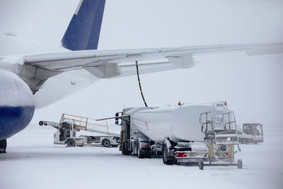 Refueling of airplane from fuel tanker at airport during snowfall. ground service on winter day.