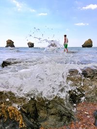 Waves splashing on rocks at beach against sky