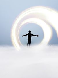 Silhouette man with light standing on cloudy sky