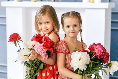 Portrait of smiling siblings with flowers standing at home