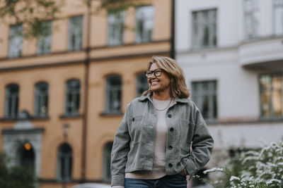 Happy senior woman wearing jacket while standing in front of building