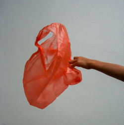 Cropped hand of person holding plastic bag against gray background