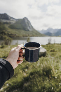 Cropped hand of person holding coffee cup against lake