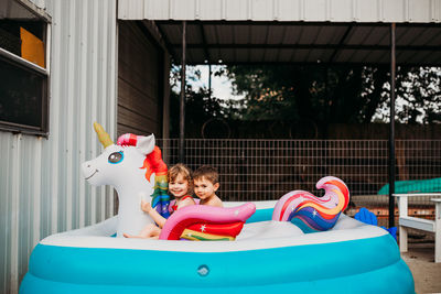 Two young kids sitting on inflatible unicorn in back yard pool