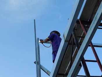 Rear view of man working against blue sky