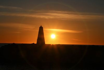 Silhouette built structure by sea against sky during sunset