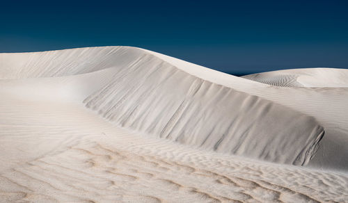 Low angle view of sand dunes against clear blue sky