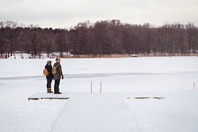 Couple standing on snow covered field against sky