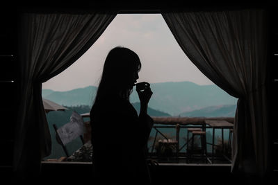 Reflection of woman photographing on mirror against window