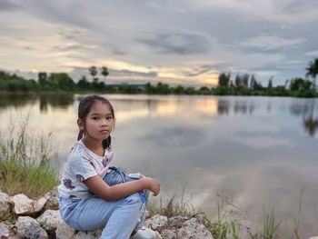 Portrait of girl sitting on lake against sky