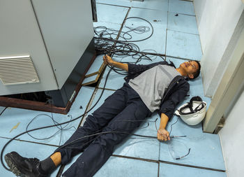 Shocked man holding cables while lying on floor by fuse box