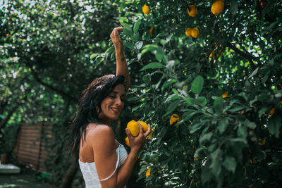 Young woman smiling while standing by tree against orange plants