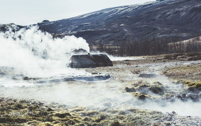Steaming geyser on field by mountain