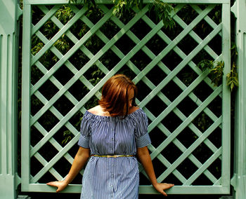 Woman standing against green fence at park