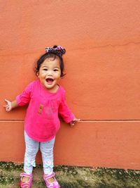 Portrait of smiling girl standing against pink wall