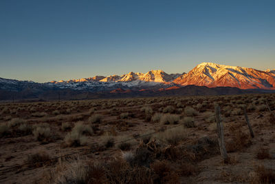 Scenic view of arid landscape at sunrise with snowy mountains against clear sky