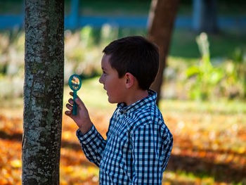 Boy holding magnifying glass by tree