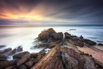 Rocks on beach against sky during sunset