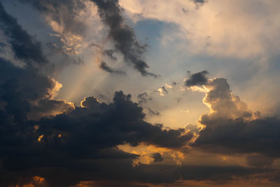 Low angle view of sunlight streaming through clouds during sunset