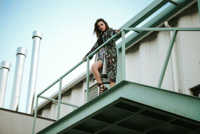 Low angle portrait of young woman standing by railing