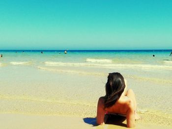 Rear view of woman sitting on beach against clear sky