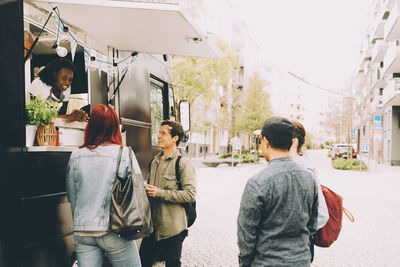 Owner with assistant talking to smiling customers by food truck on street