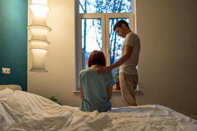 Rear view of young woman sitting on bed at home