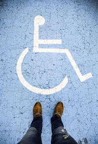 Low section of man standing on road with wheelchair access sign