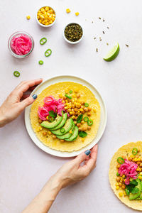 Hand of crop anonymous female touching tasty taco with ripe avocado slices and chickpea filling served on table