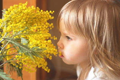 Close-up side view of cute baby girl smelling yellow flowering plants at home