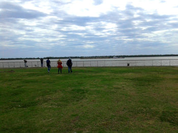 People playing soccer on beach against cloudy sky