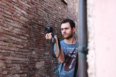 Portrait of young man standing against brick wall