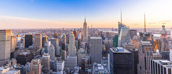 Empire state building amidst cityscape at manhattan during sunset