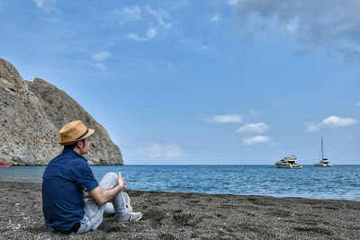 Man looking at sea while sitting at beach against sky