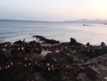 Love locks hanging on rusty metallic chain by rocky shore against sky