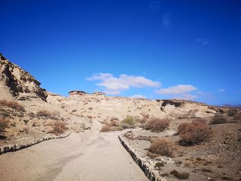 Scenic view of road by mountains against blue sky