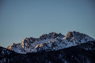 Low angle view of snowcapped mountains against clear blue sky