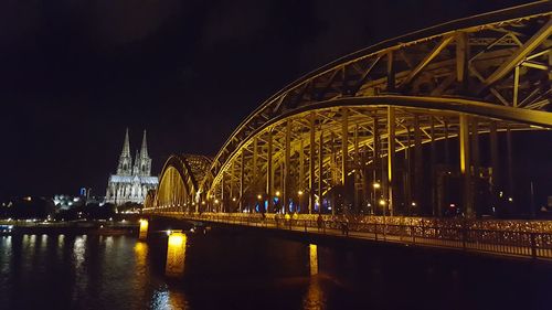 Illuminated hohenzollern bridge over river rhine by cologne cathedral against clear sky at night