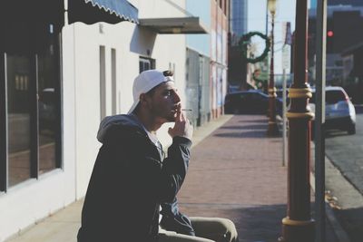 Side view of young man smoking cigarette on sidewalk