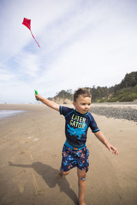 Young boy running kite along the beach with determination.