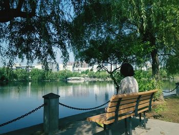 Rear view of woman sitting on pier over lake