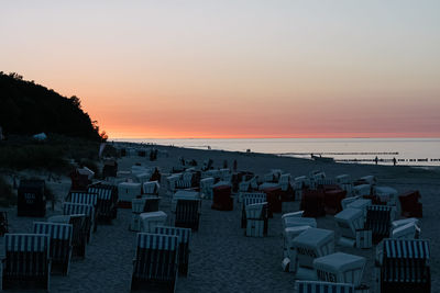 Hooded chairs on beach against sky during sunset